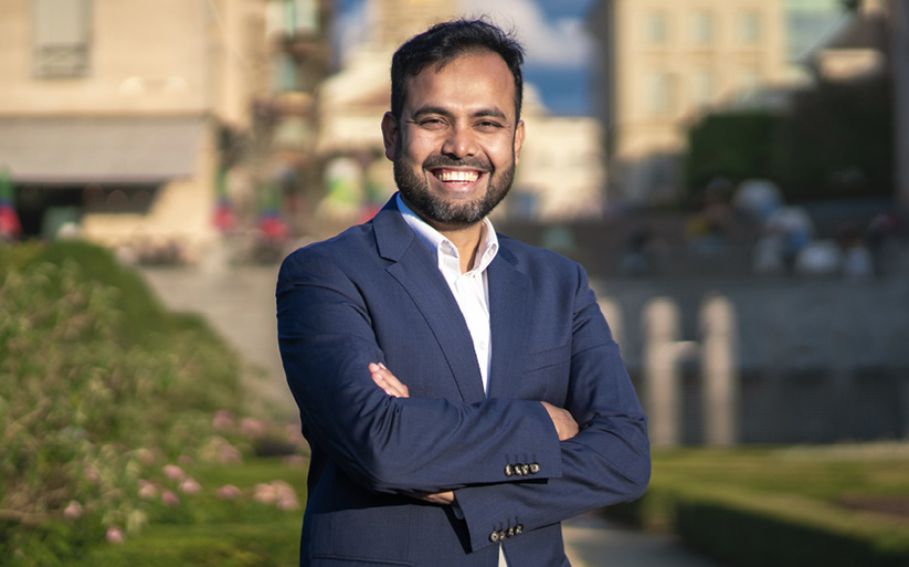 Gofran Chowdhury stands, arms folded. Blurred cityscape in the background.