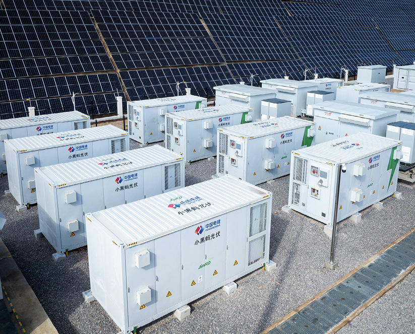 Batteries in white containers, with solar panels in the background.