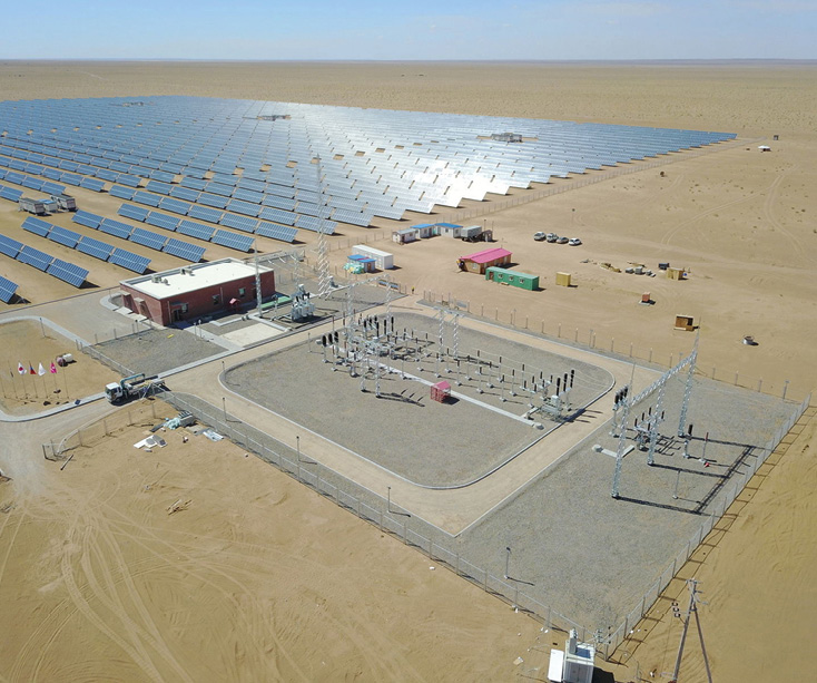 Rows of solar panels and an electrical substation surrounded by a desert landscape.